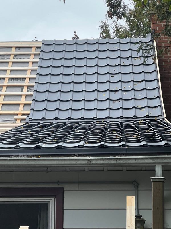 Dark metal roof in a tile profile, with the next section strapped
