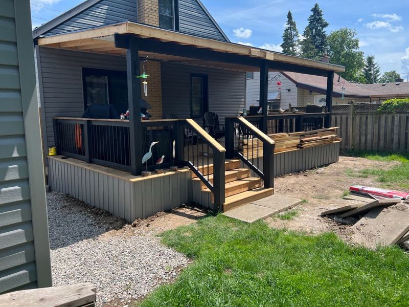 Covered wood deck with black railings, steps and the roof framing exposed